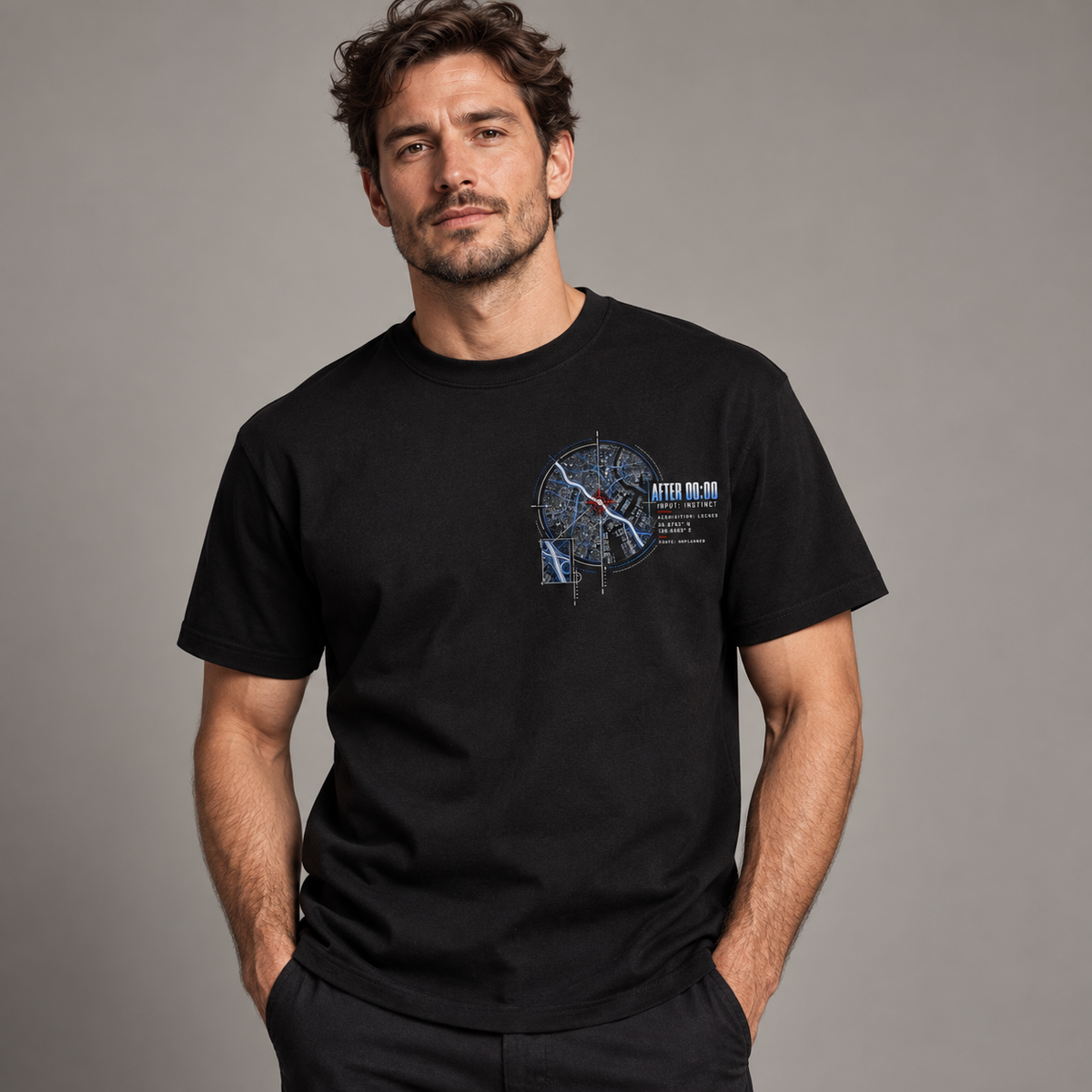 A man wearing a black short-sleeve graphic t-shirt with a detailed map design on the left chest, posed against a neutral gray studio background.