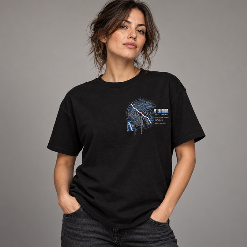 A woman wearing a black graphic t-shirt with a compass design and text that reads 'AFTER 00:00', paired with dark gray jeans, against a solid gray studio background.