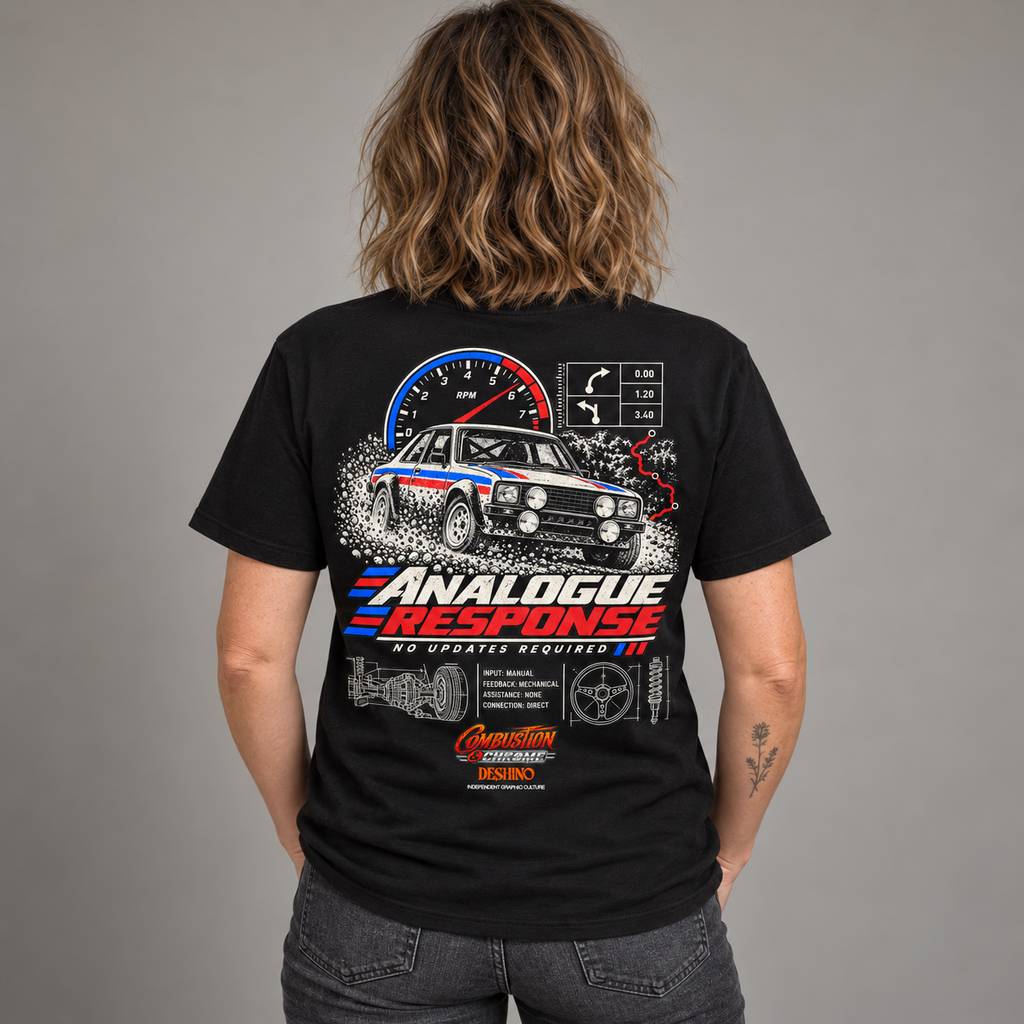 A person shown from the back wearing a black graphic T-shirt with a large car and speedometer print, paired with dark gray jeans, against a plain gray studio background.