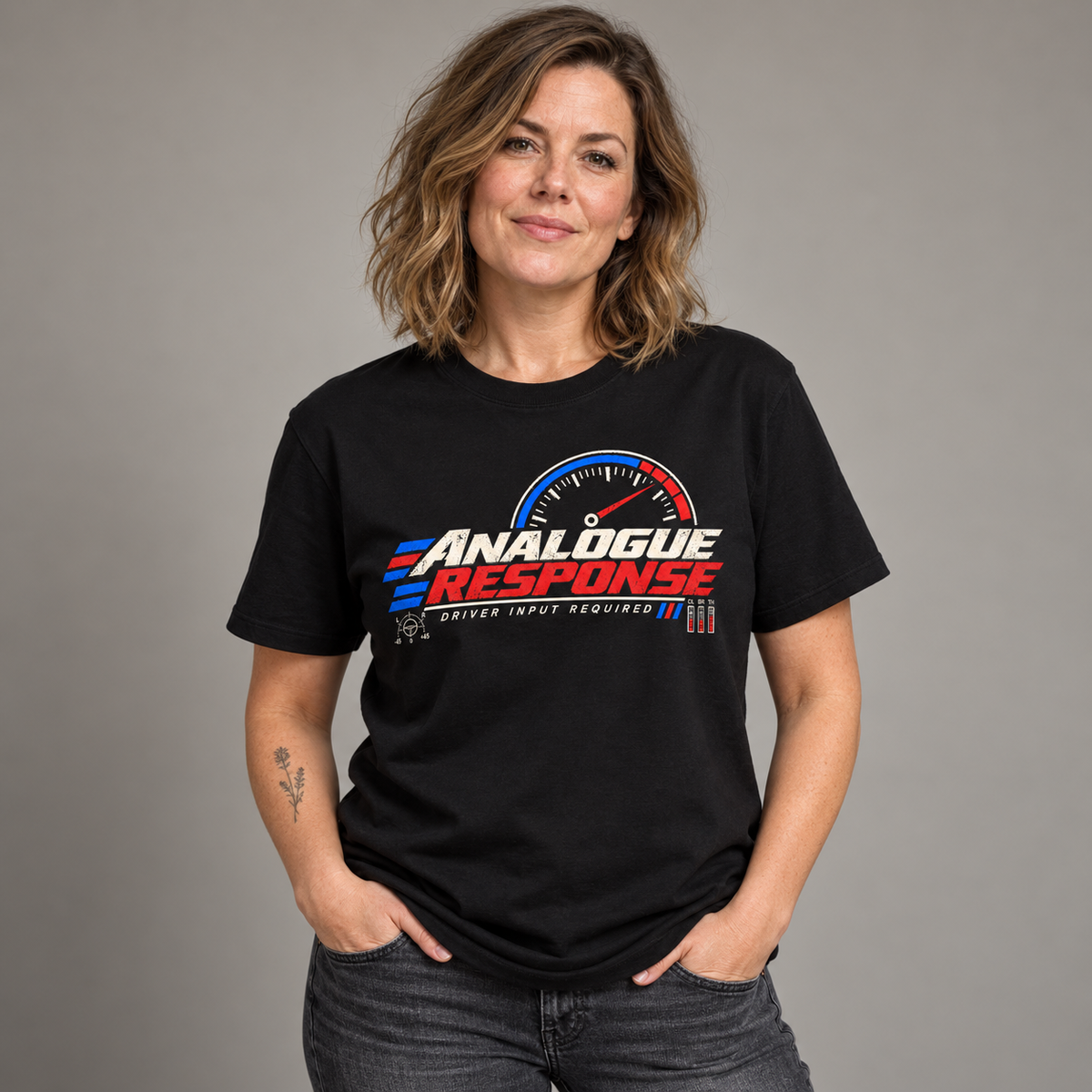 A woman wearing a black graphic t-shirt with a red, white, and blue 'Analogue Response' speedometer design, standing against a neutral gray background.