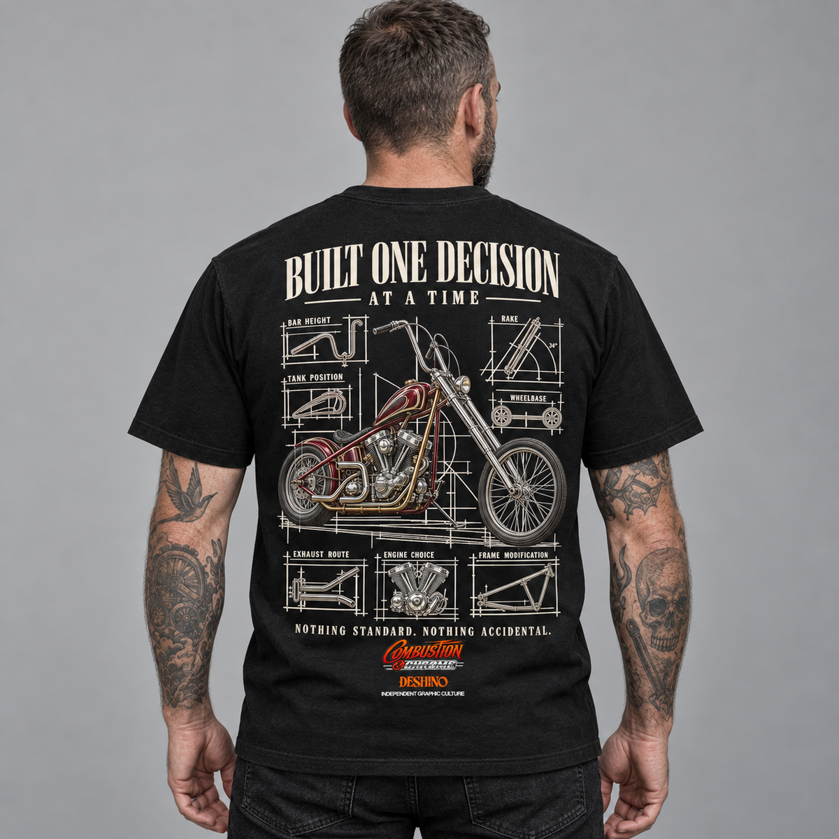 A man viewed from behind wearing a black graphic t-shirt. The back of the shirt features a large white and red technical blueprint-style illustration of a chopper motorcycle, with the text 'BUILT ONE DECISION AT A TIME'.