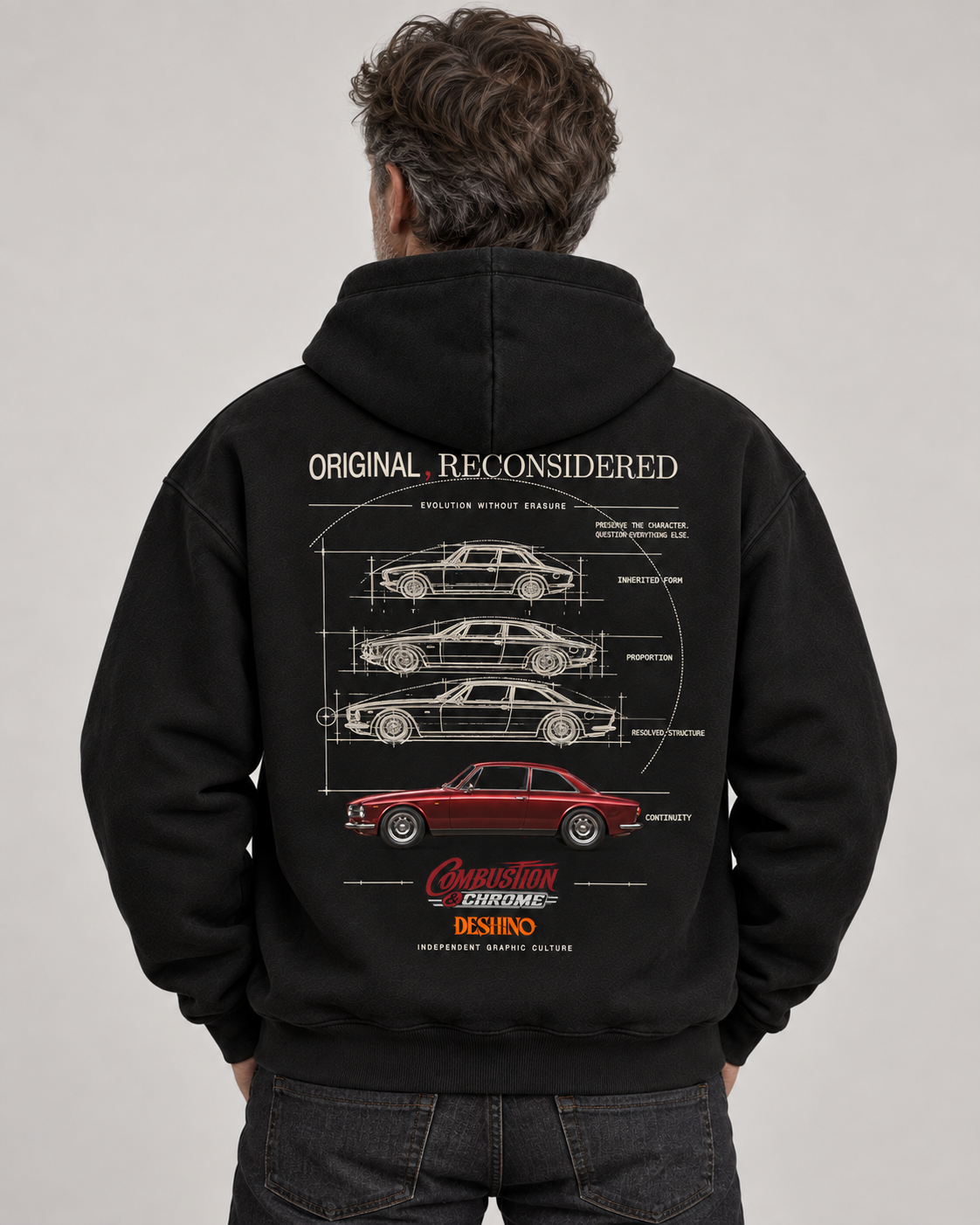 A man viewed from behind wearing a black hoodie with a large white car schematic graphic and a red car illustration on the back. The hoodie features the text 'ORIGINAL RECONSIDERED'.