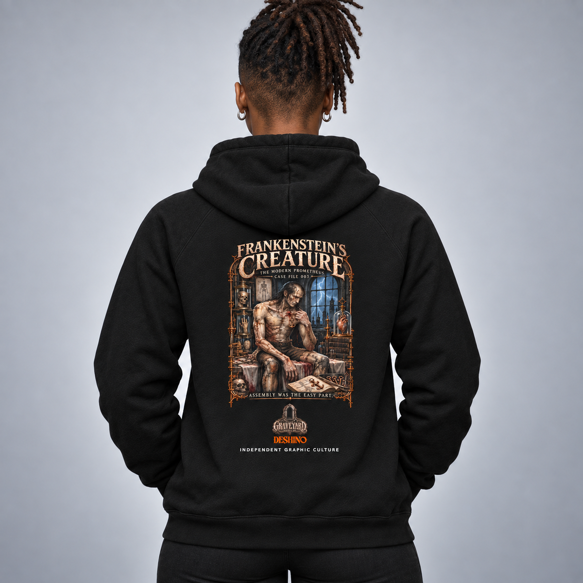 A person shown from the back wearing a black hoodie with a large illustrated graphic on the back. The graphic reads 'Frankenstein's Creature' and features a detailed artwork in brown, beige, and blue tones.