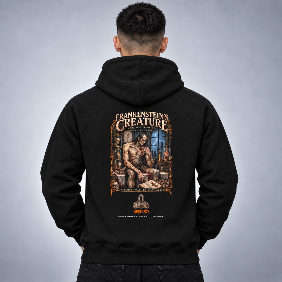 A man viewed from behind wearing a black hoodie with a large graphic print on the back. The graphic features the text 'FRANKENSTEIN'S CREATURE' and an illustration of a muscular creature in a laboratory.