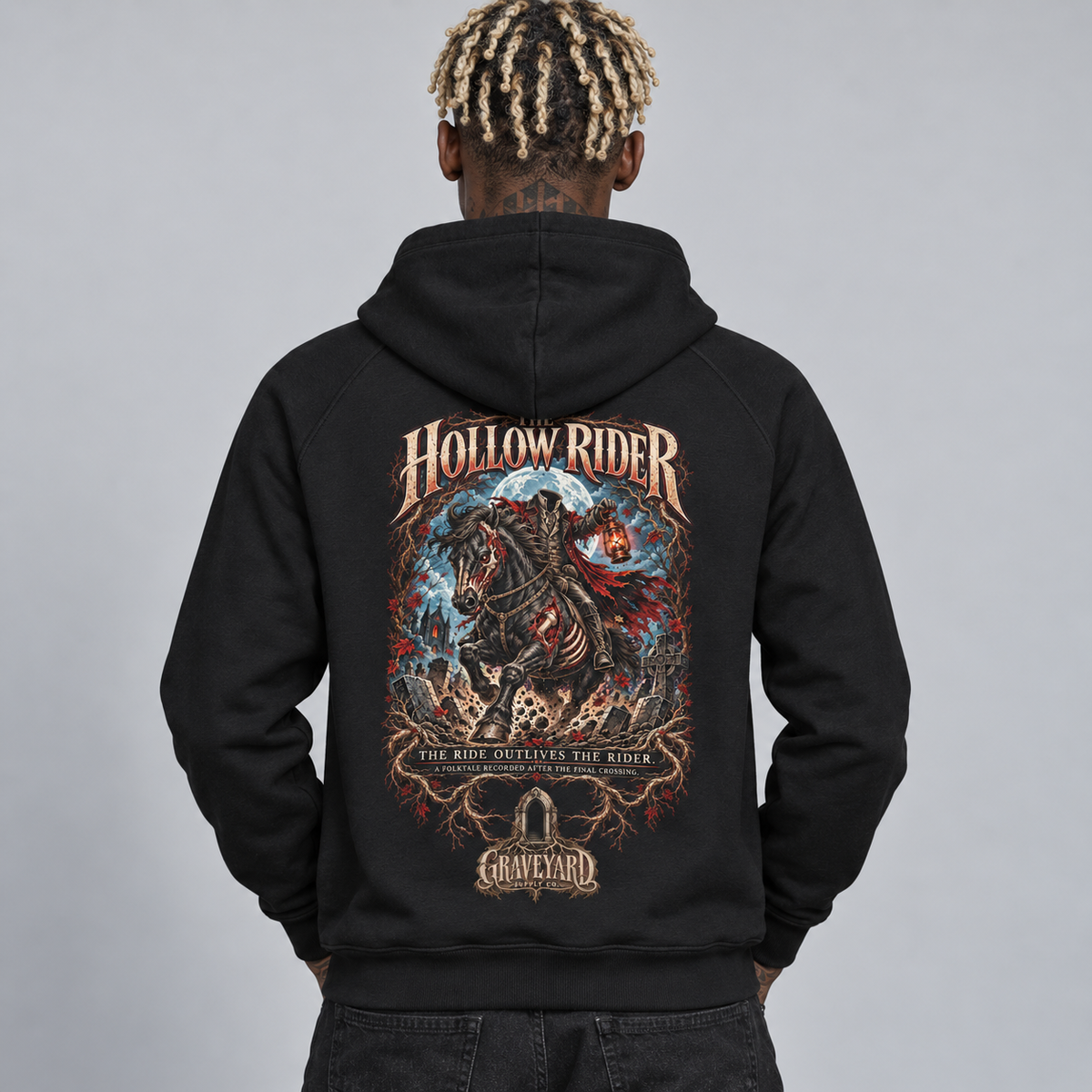 A man viewed from behind wearing a black pullover hoodie with a large, detailed graphic print on the back. The graphic features the text 'HOLLOW RIDER' and 'THE RIDE OUTLIVES THE RIDER' with a dark fantasy illustration of a headless rider on a horse, and a 'Graveyard' logo at the bottom. 