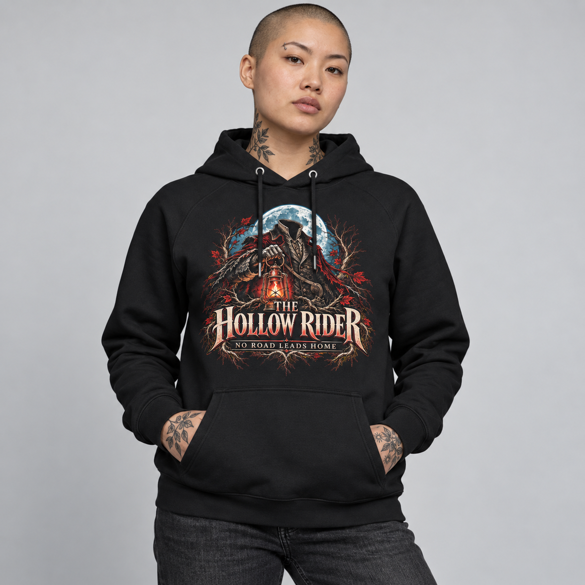 A model wearing a black pullover hoodie with a detailed graphic on the chest that reads 'THE HOLLOW RIDER' and 'NO ROAD LEADS HOME'. The graphic features a dark gothic scene with a figure, a full moon, and red/orange light effects.