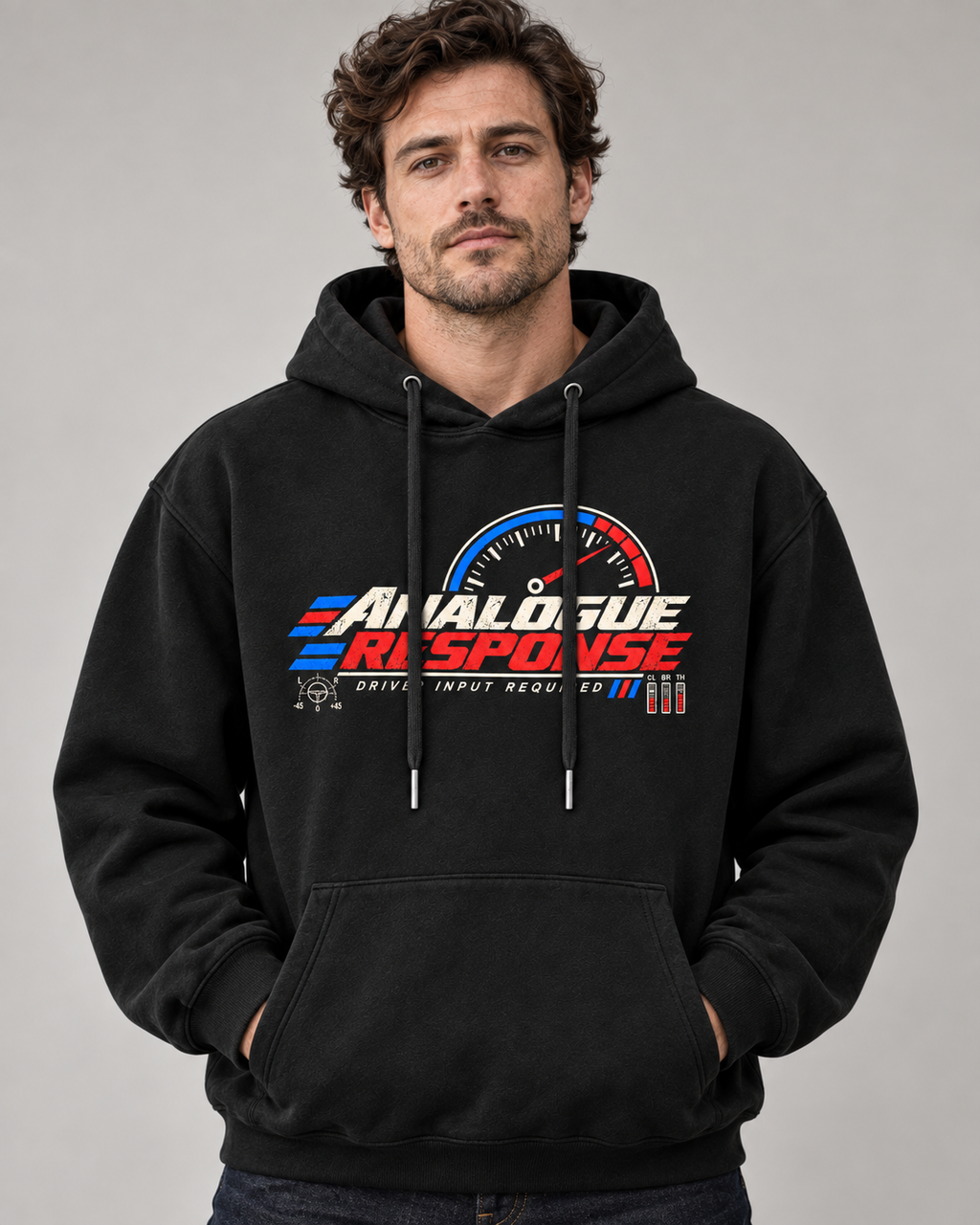 A man wearing a black pullover hoodie with a large 'ANALOGUE RESPONSE' graphic on the chest, featuring a red, white, and blue speedometer design, against a plain gray studio background.