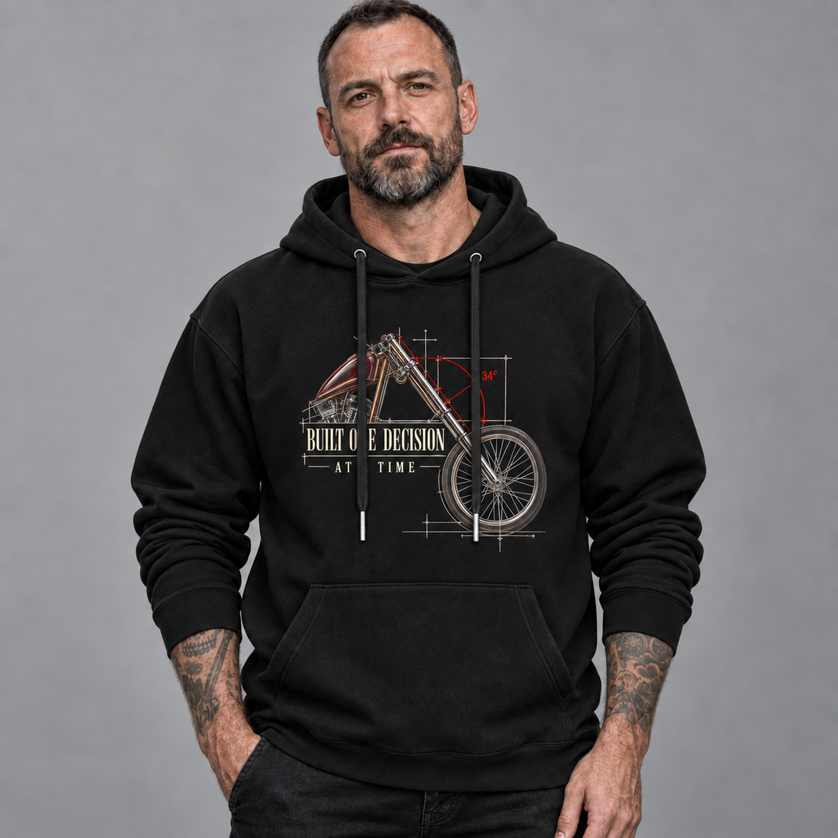 A man wearing a black pullover hoodie with a graphic print of a motorcycle in blueprint style and the text 'BUILT ONE DECISION AT TIME'.