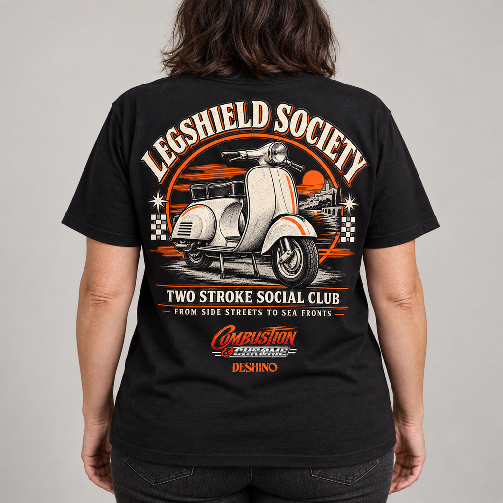 A person shown from the back wearing a black graphic T-shirt with a large retro scooter design and text reading 'Legshield Society' and 'Two Stroke Social Club.' The shirt has prominent orange, white, and beige print details on a light gray studio background.