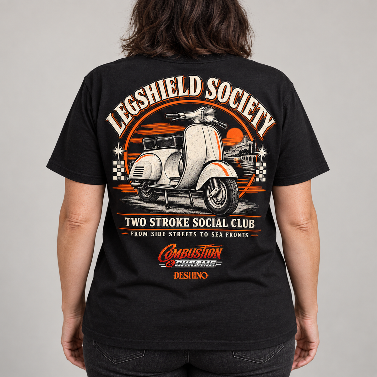 A person shown from the back wearing a black graphic T-shirt with a large retro scooter design and text reading 'Legshield Society' and 'Two Stroke Social Club.' The shirt has prominent orange, white, and beige print details on a light gray studio background.