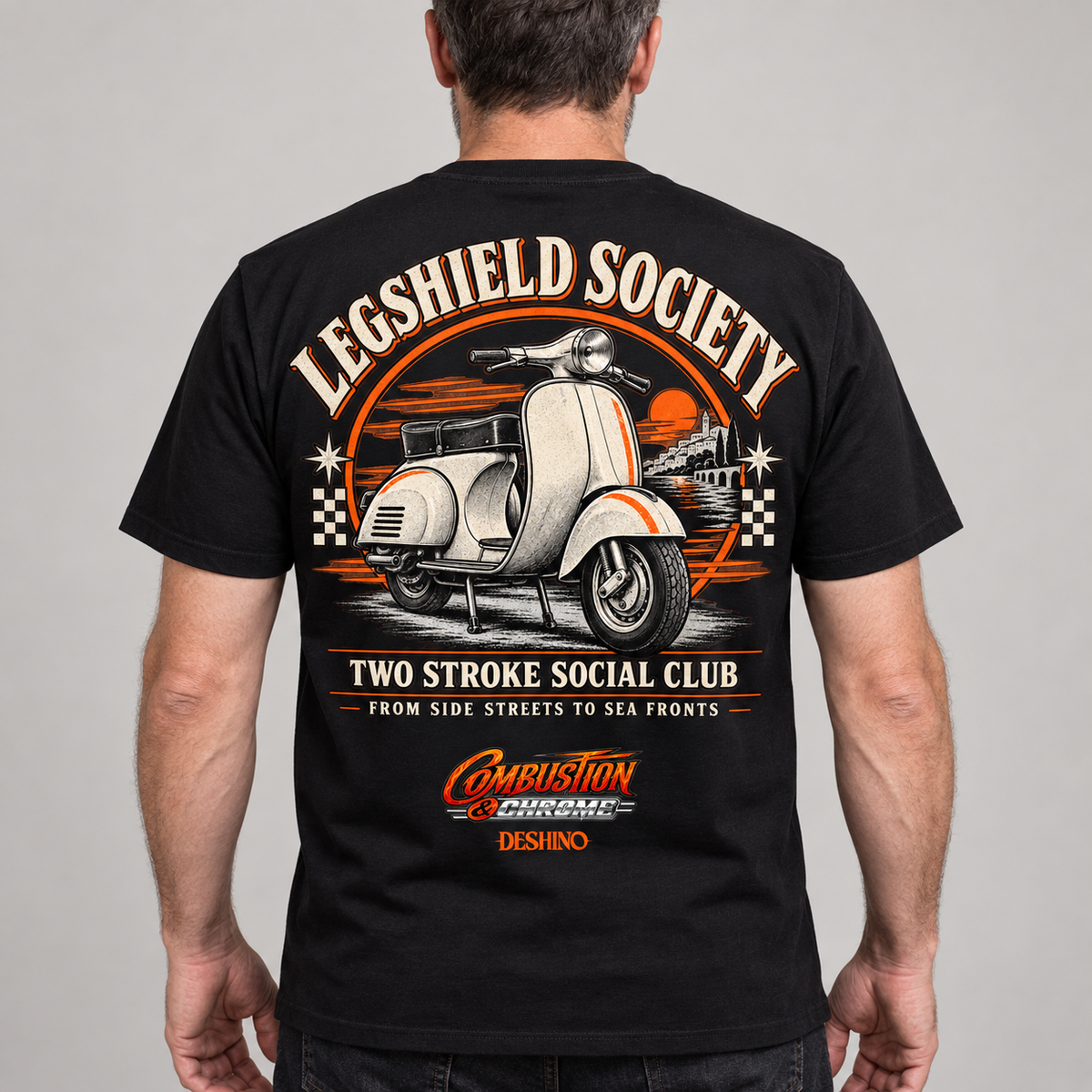 A man viewed from the back wearing a black t-shirt with a large vintage-style graphic on the back. The graphic features a white scooter, orange and beige text reading 'LEGSHIELD SOCIETY' and 'TWO STROKE SOCIAL CLUB', and a 'Combustion & Chrome' logo near the bottom.