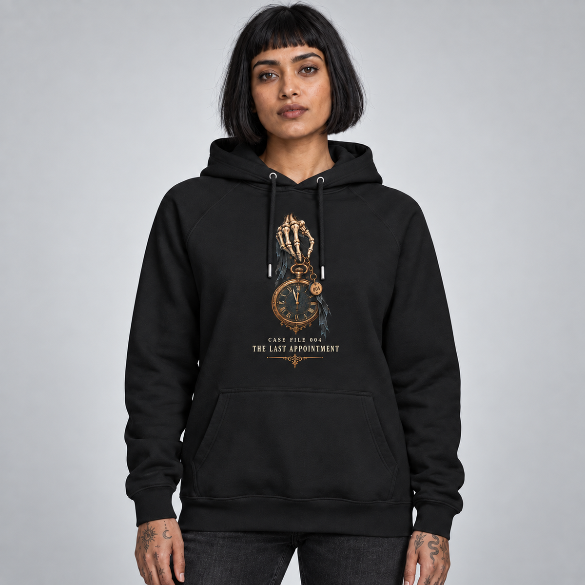 A woman with short black hair modeling a black pullover hoodie with a gothic skeleton hand and clock graphic on the chest, reading 'THE LAST APPOINTMENT'. She is standing against a neutral grey studio background.