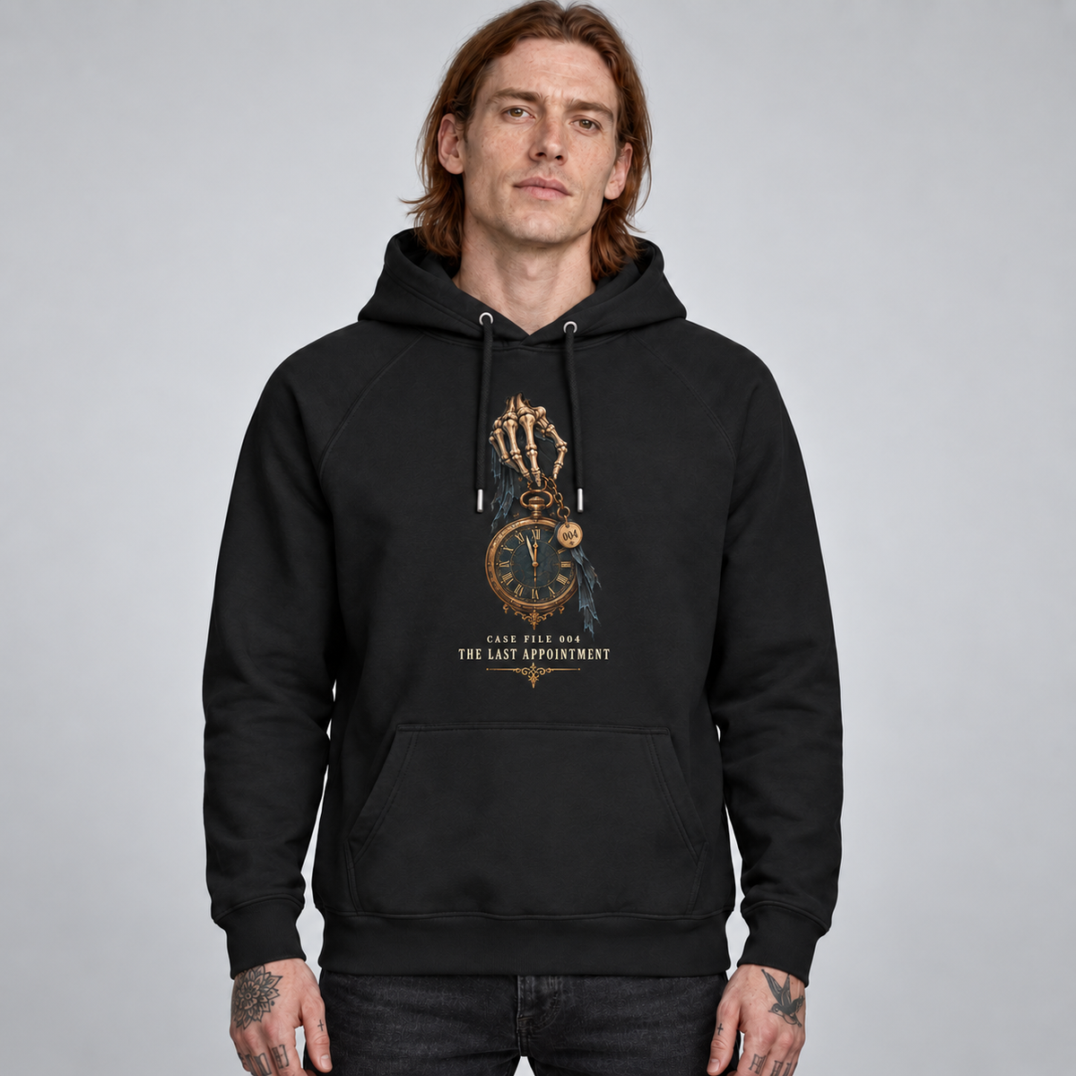 A man wearing a black pullover hoodie with a gothic skeleton hand graphic holding a pocket watch, with the text 'The Last Appointment' printed on the chest, set against a plain grey studio background.