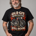 A man wearing a black graphic t-shirt with a vintage-style motorcycle print and the text 'OLD GIT MOTOR CYCLE CLUB' and 'STILL KICKING'.