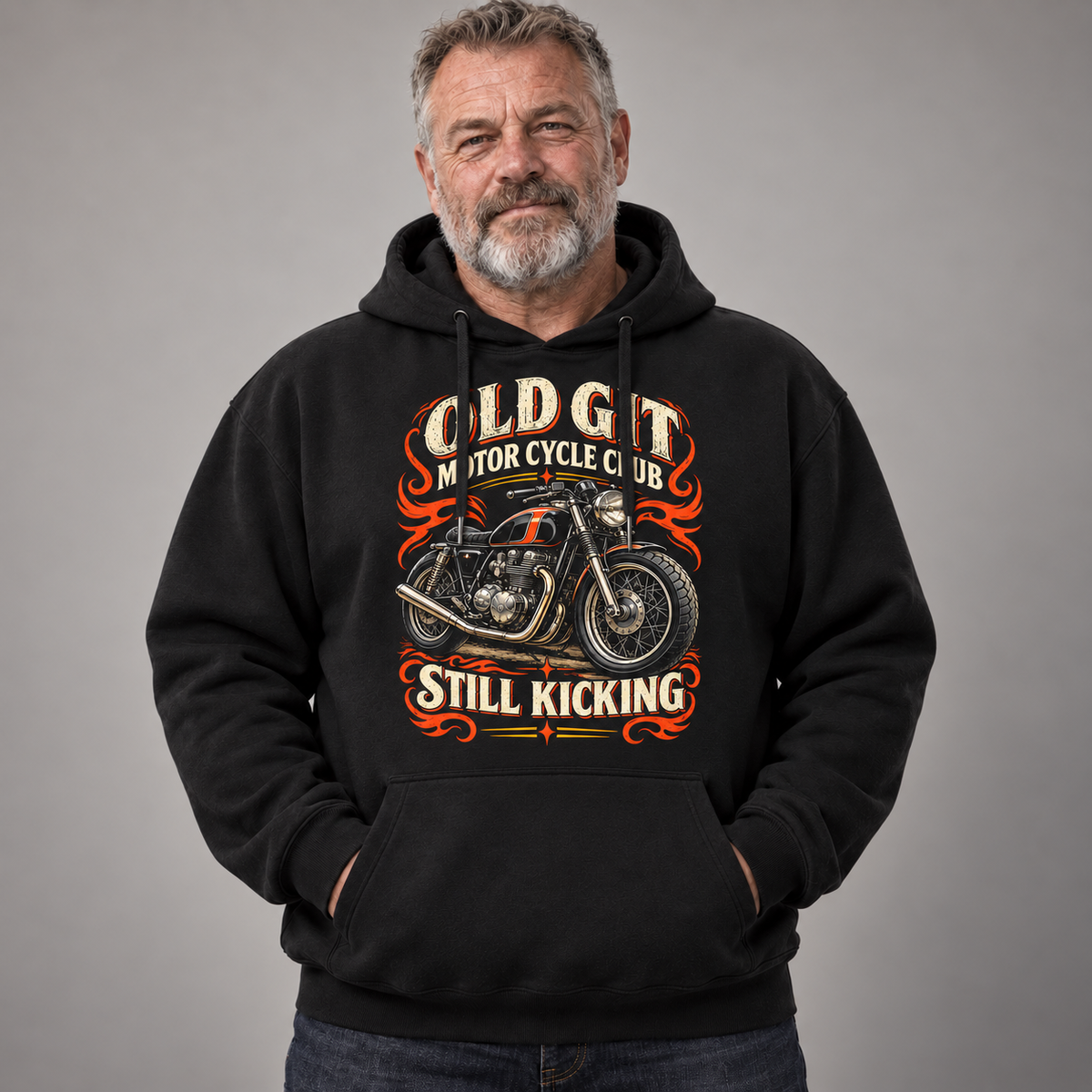A man wearing a black pullover hoodie with a vintage-style graphic of a motorcycle and the text 'OLD GIT MOTORCYCLE CLUB STILL KICKING' on a plain gray studio background.