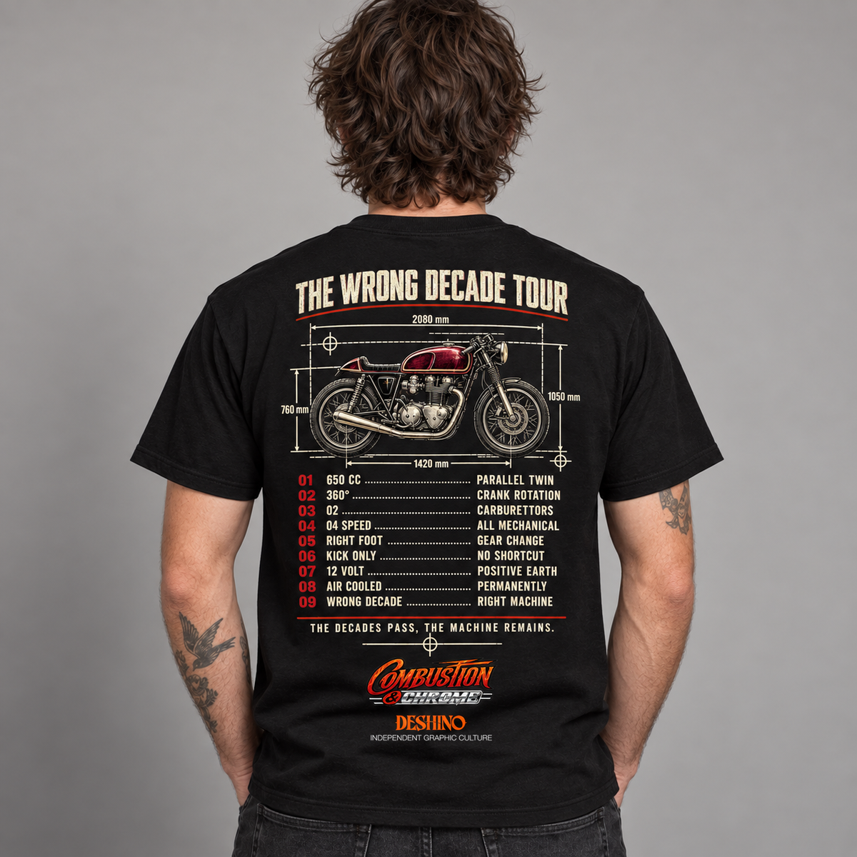 A man viewed from behind wearing a black t-shirt with a detailed back graphic. The graphic features a red and silver motorcycle with dimension lines, the text 'THE WRONG DECADE TOUR', a numbered list, and the 'Combustion & Chrome' & 'Deshino' logos.